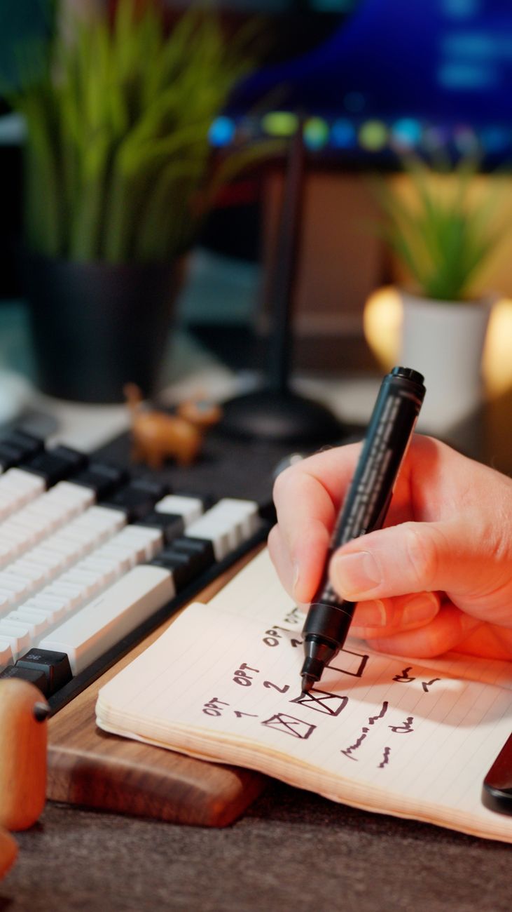 hand marking tasks in notebook near keyboard