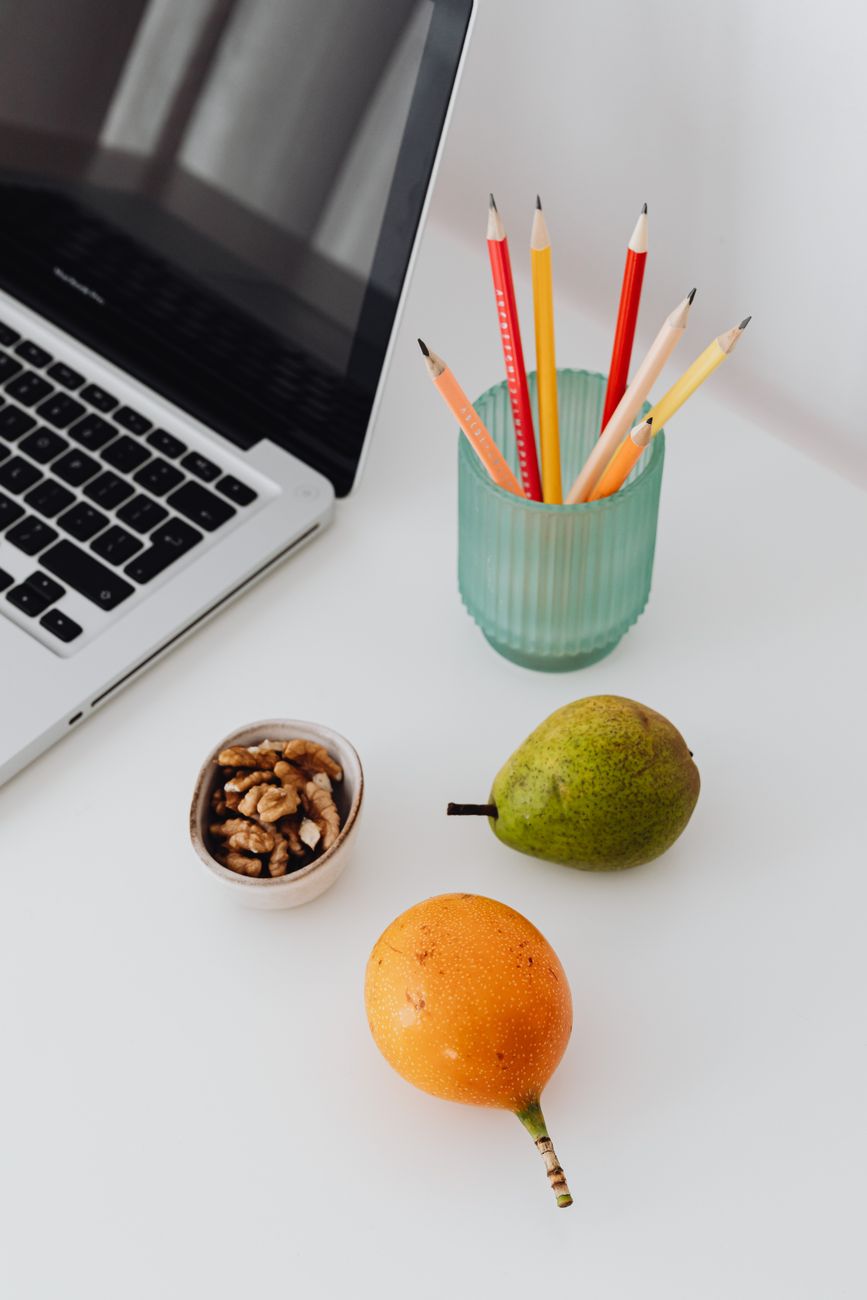 top view of a white desk with fruits pencils and laptop