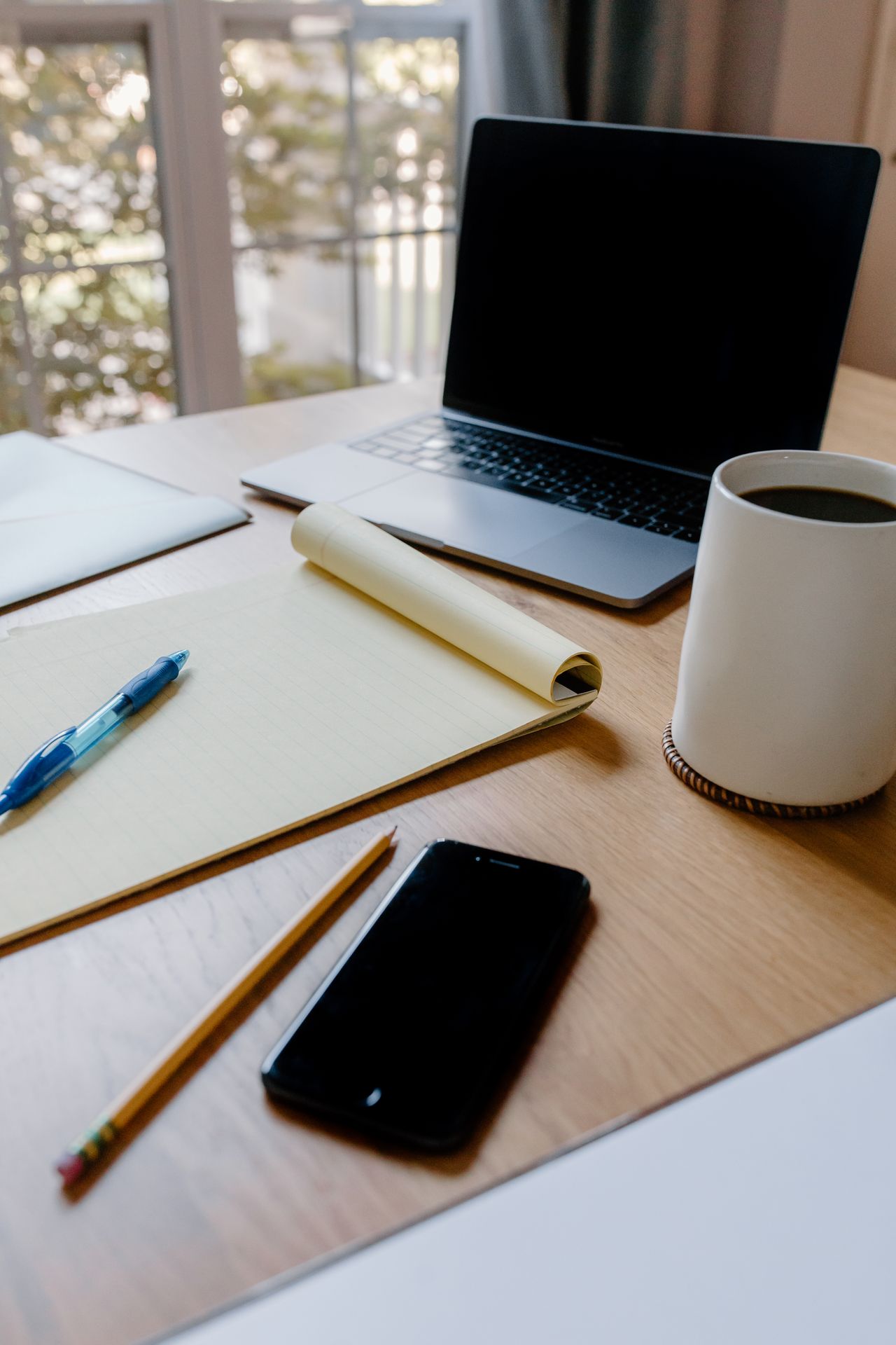 Laptop, open notebook, pen, phone and mug on a wooden table.