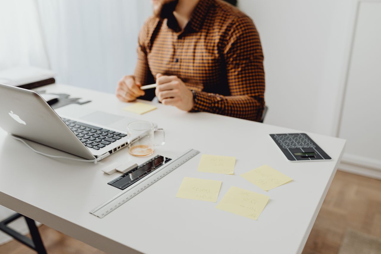 Person at a desk with a laptop, notebook, calculator and sticky notes.