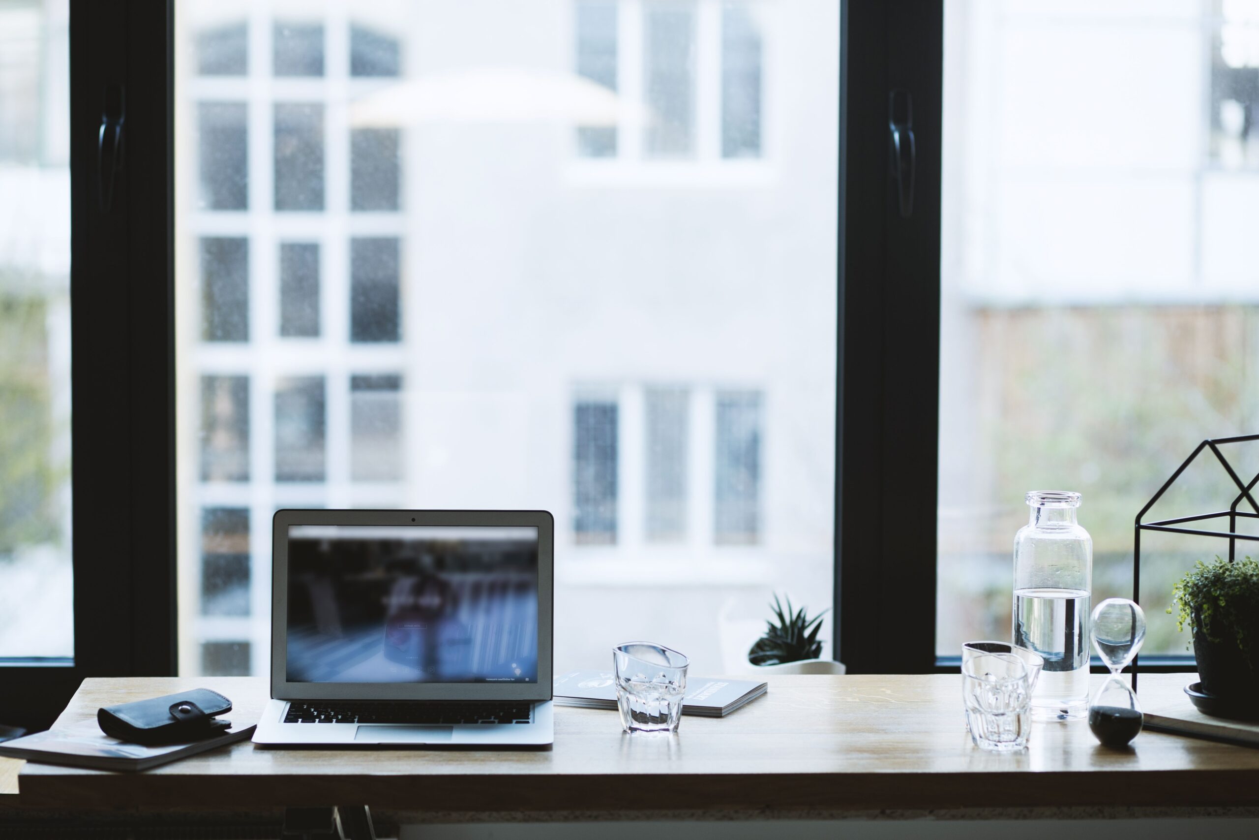 Laptop and glass on a desk beside a large window.