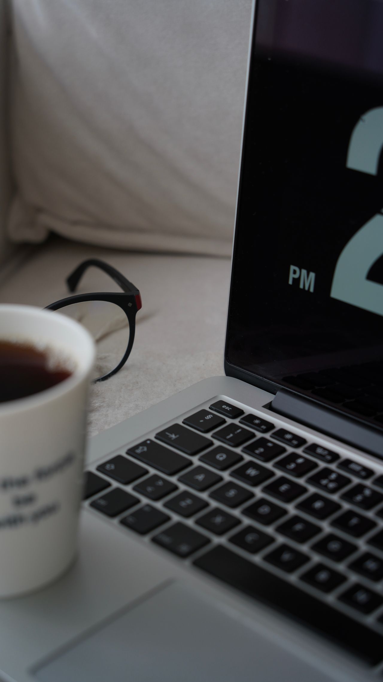 Close view of a laptop, mug and eyeglasses on a table.