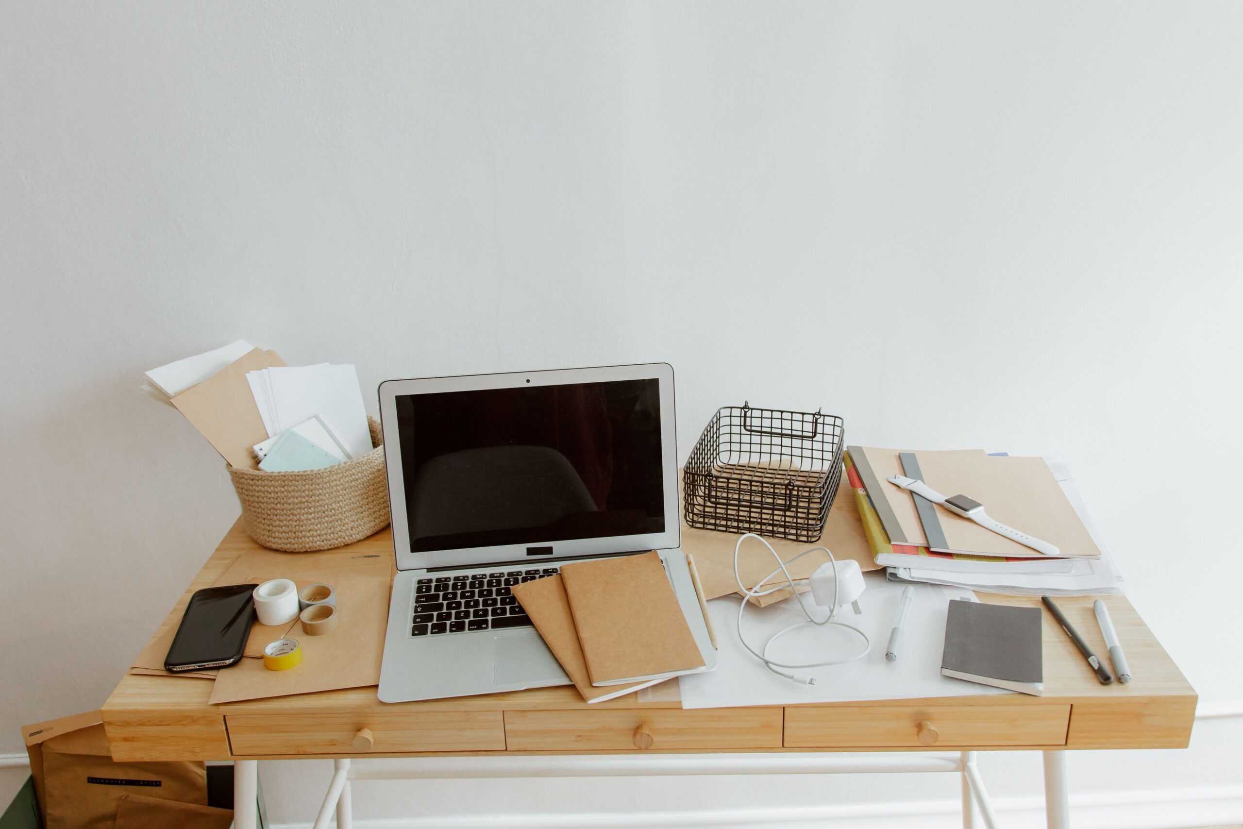 Laptop, notebooks, loose papers and stationery on a desk.