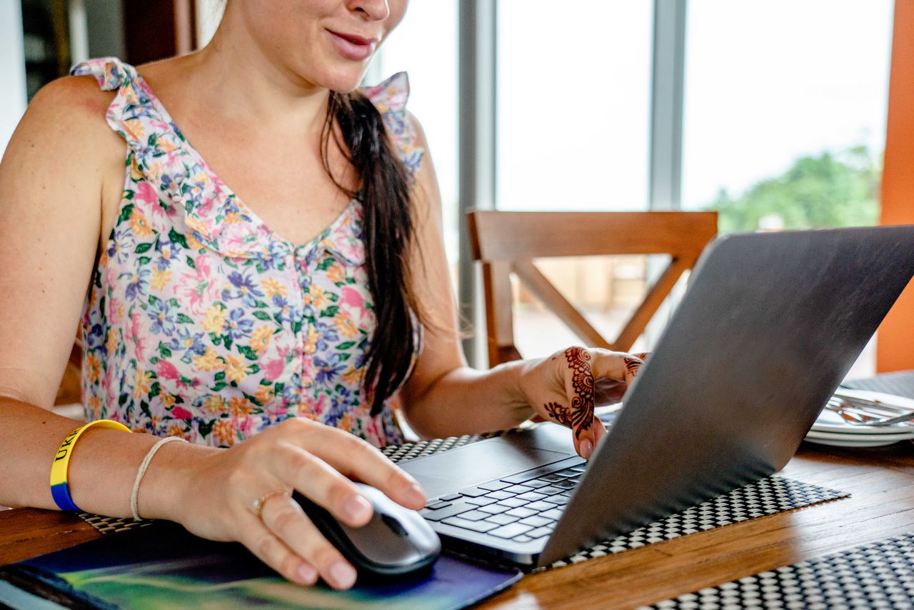 Person in floral clothing using a laptop and mouse at a table.