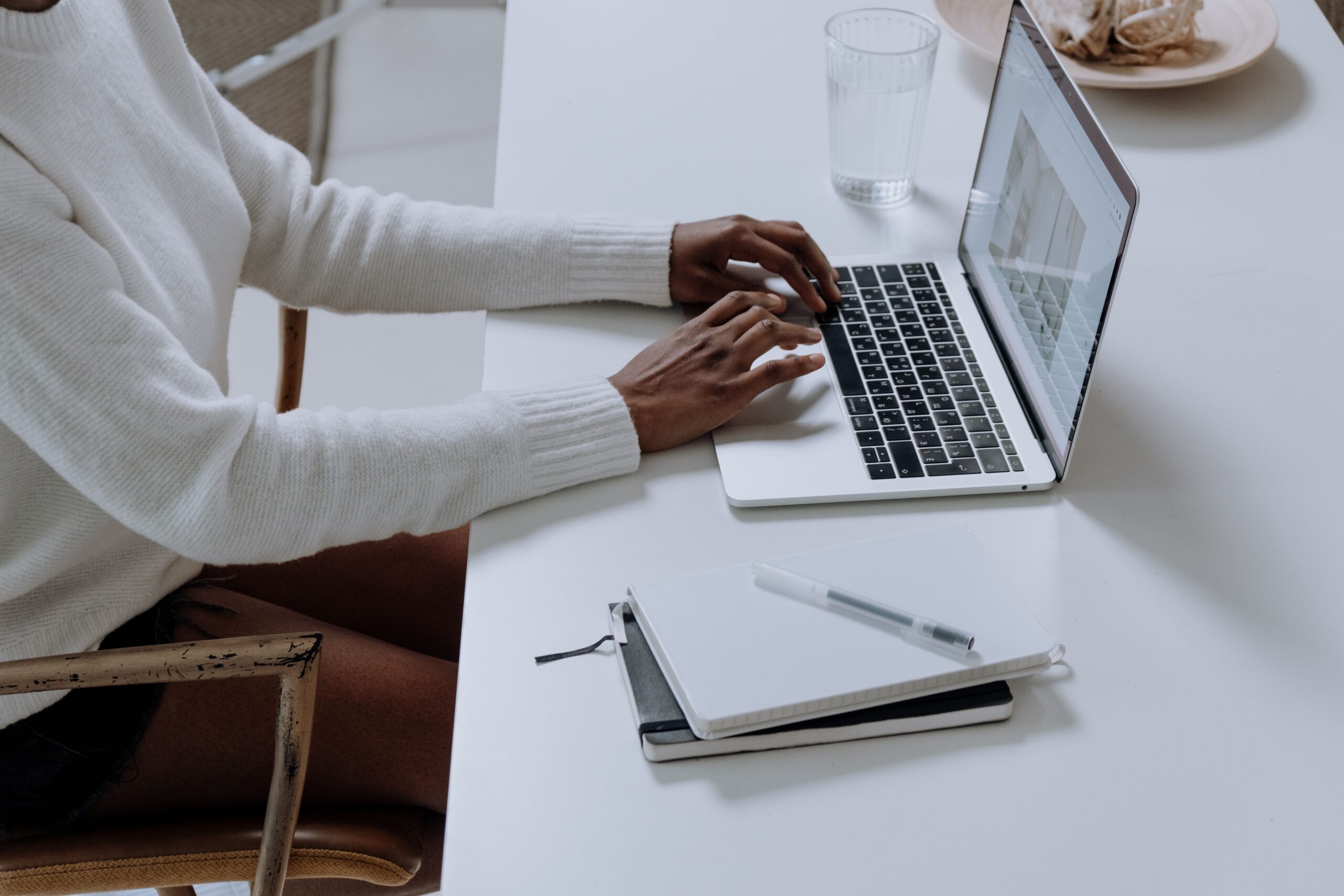 Hands typing on a laptop beside a notebook.