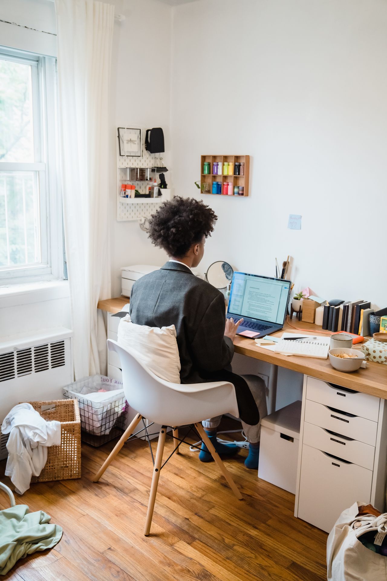 Person using a laptop at a desk beside books and a window.