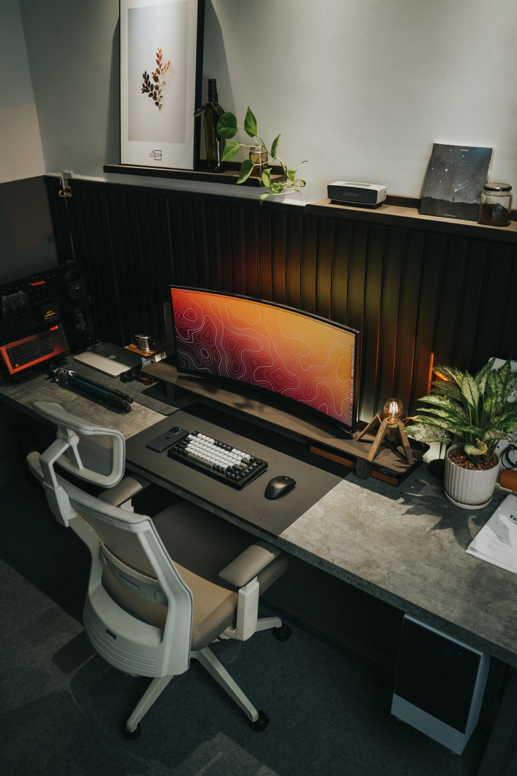 Desk with a wide monitor, keyboard, chair and plants.