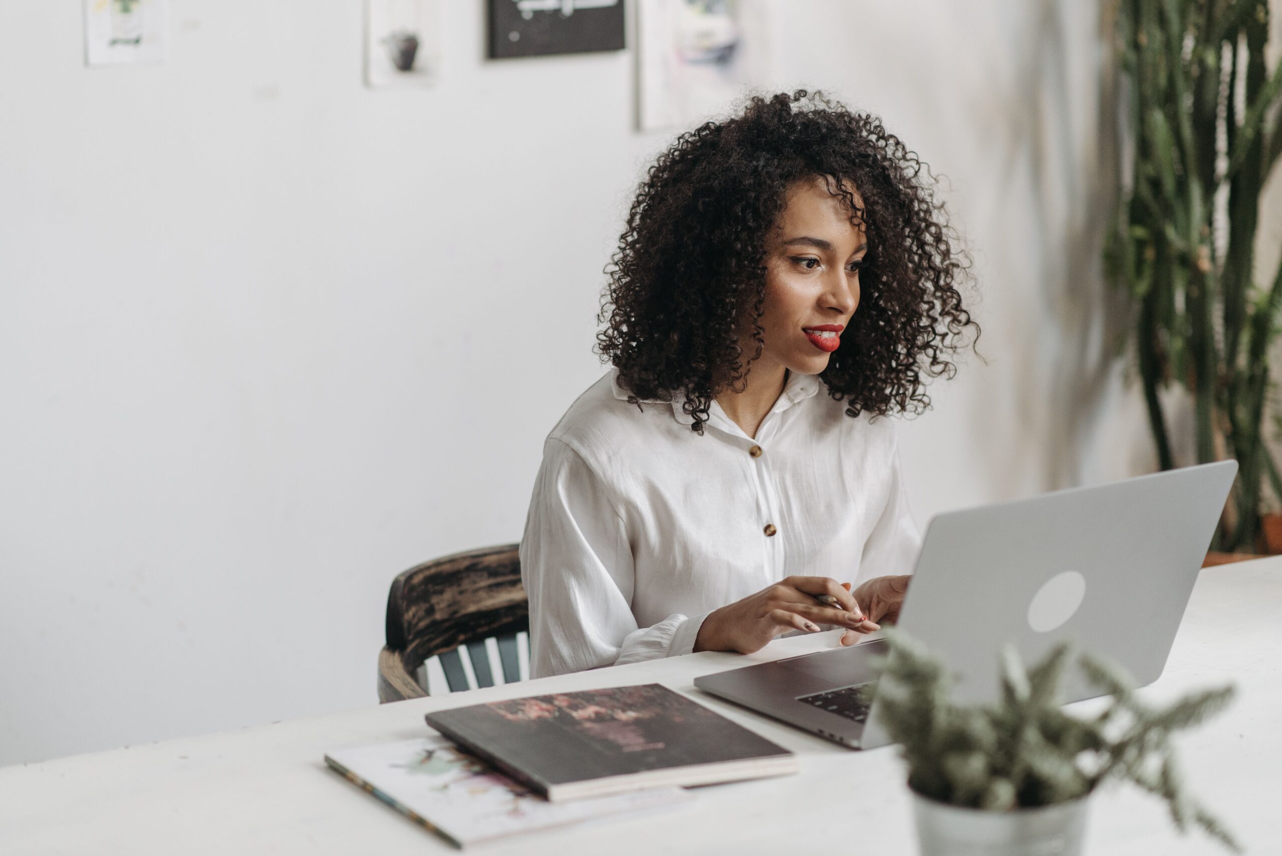 Person with curly hair using a laptop beside papers.